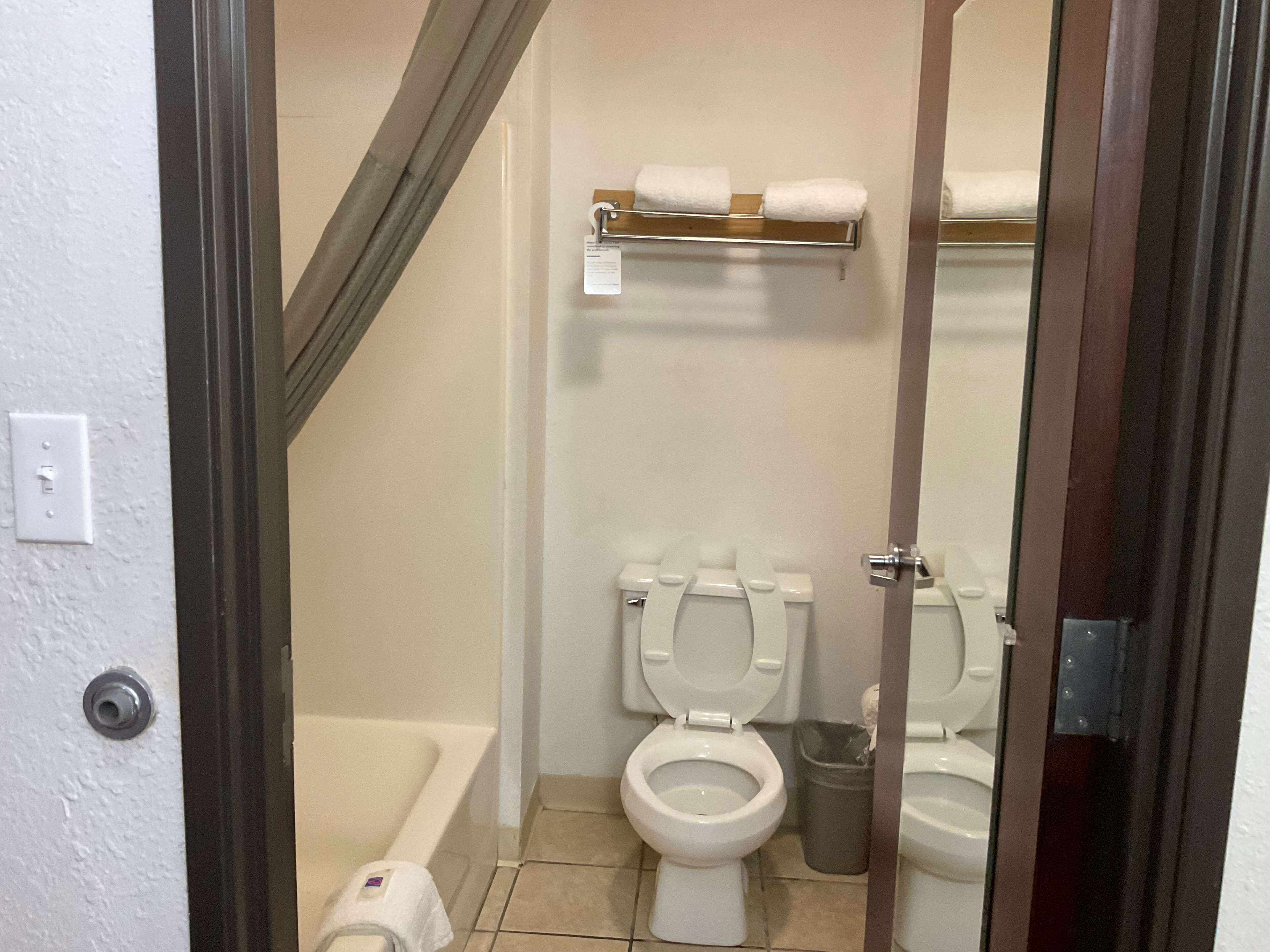 A bathroom with two toilets, a bathtub, a towel rack, and a trash bin.