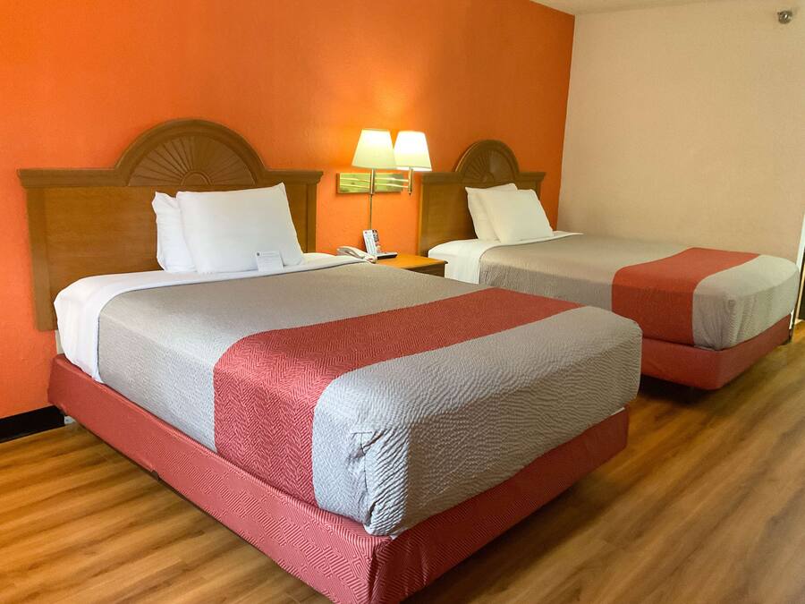 A hotel room with two beds, each with a headboard, a nightstand, a lamp, and a telephone.