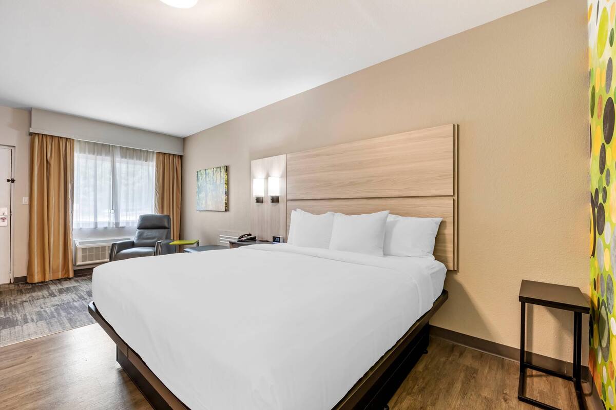 Ein Hotelzimmer mit einem großen Bett, einem Schreibtisch, einem Stuhl und einem fenster mit Vorhängen.