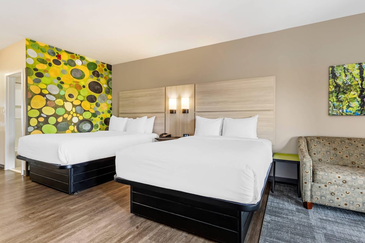 Ein Hotelzimmer mit zwei Betten, einem Sofa, einer farbenfrohen abstrakten Wand und einem kleinen Tisch.