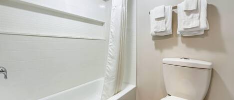 Et badeværelse med et hvidt badekar, en bruseforhæng, et toilet og to håndklæder hængende på væggen.