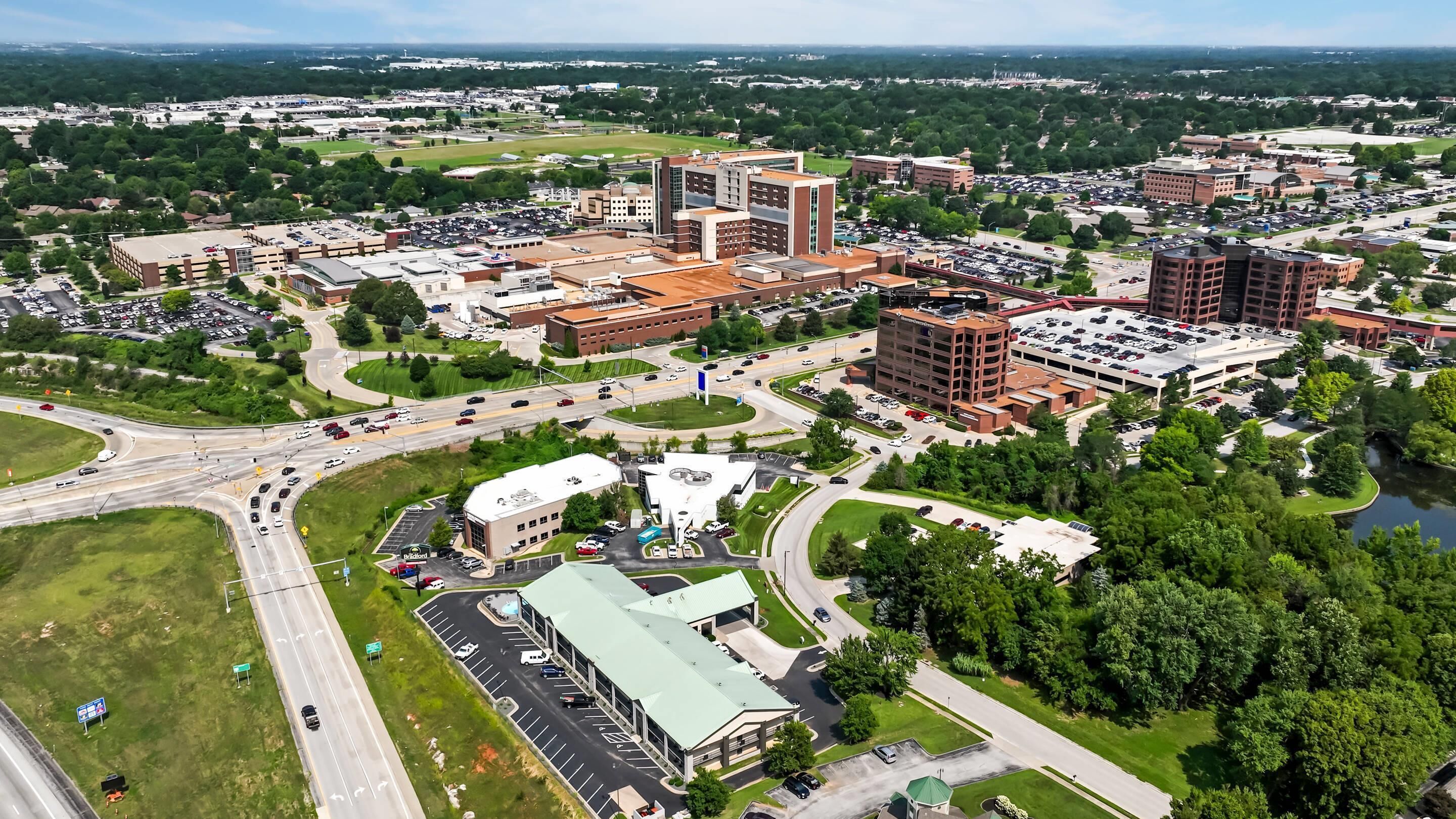 An aerial view of a cityscape with multiple buildings, roads, and a parking lot.