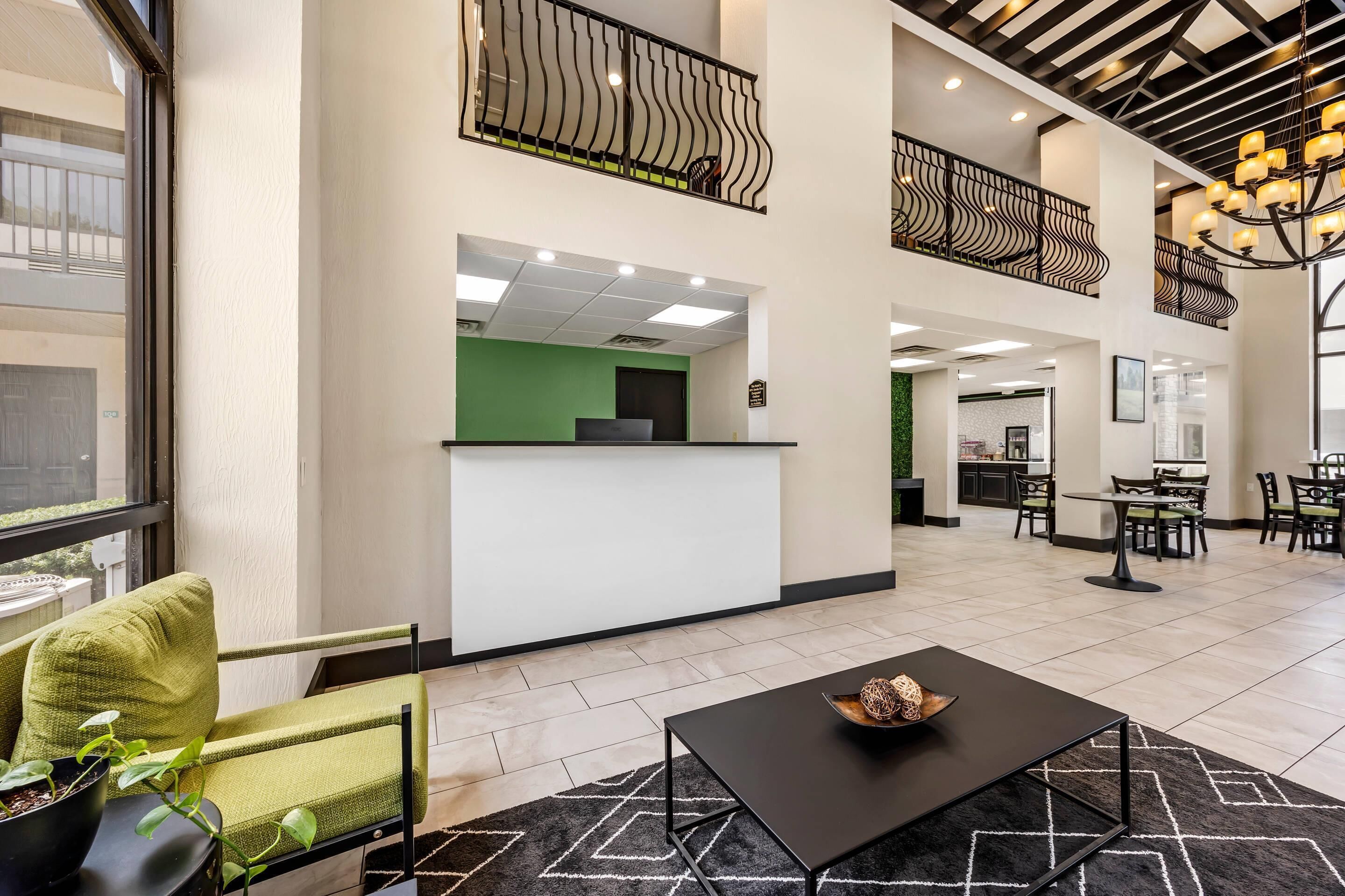 Un amplio vestíbulo con mostrador de recepción, zona de estar y escalera que conduce a un nivel superior.