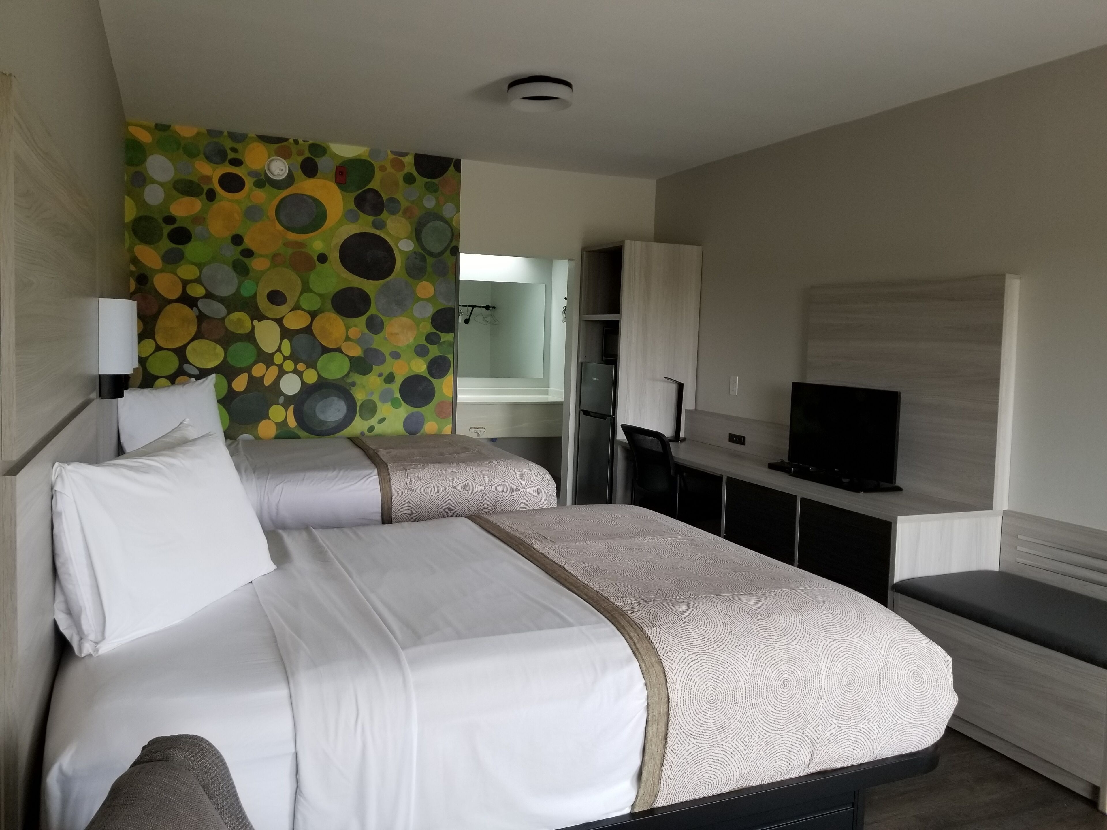 A hotel room with a bed, a desk, a TV, and a bathroom visible through an open door.
