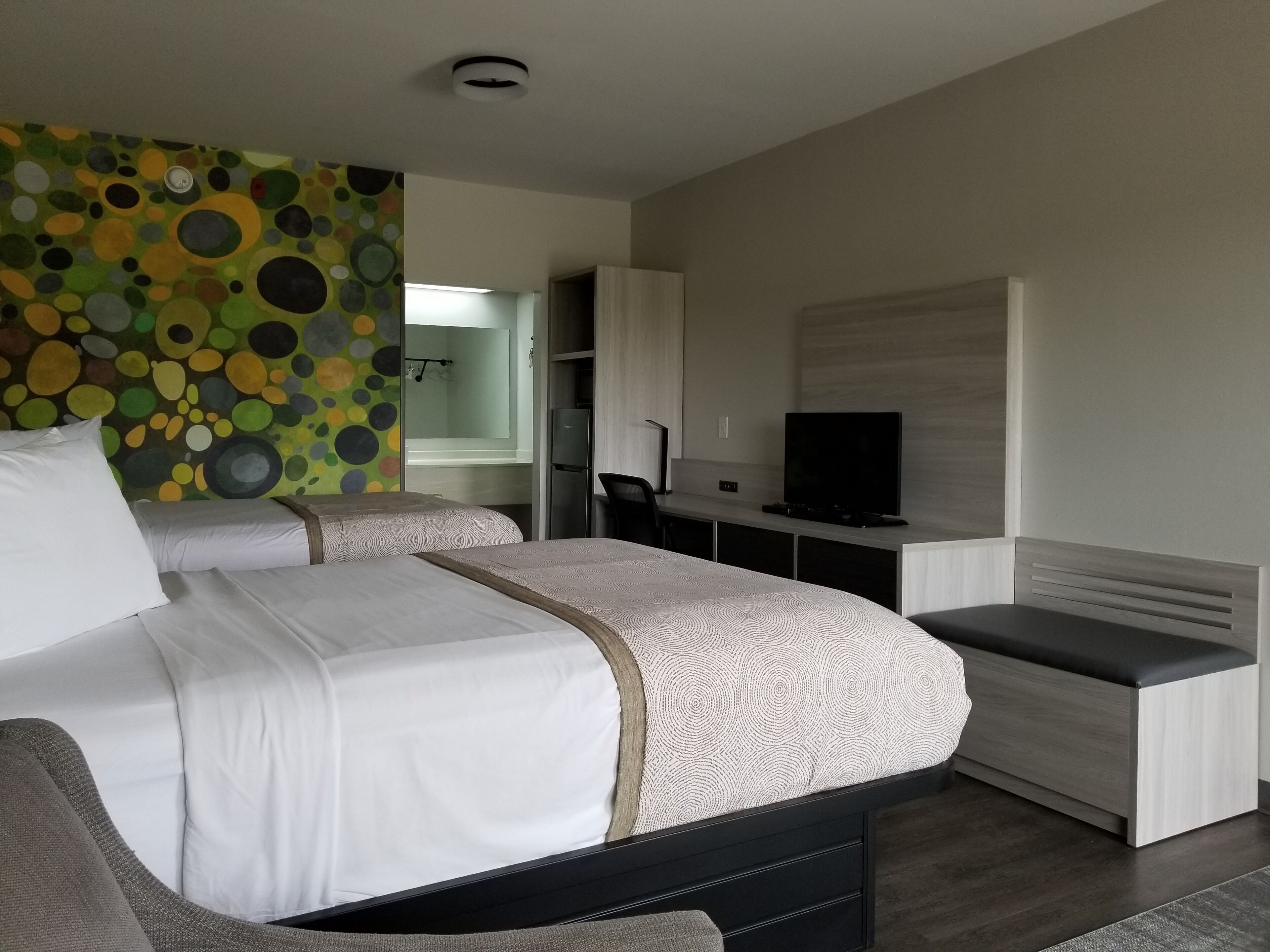 A modern hotel room with a large bed, a desk with a television, and a colorful wall decoration.