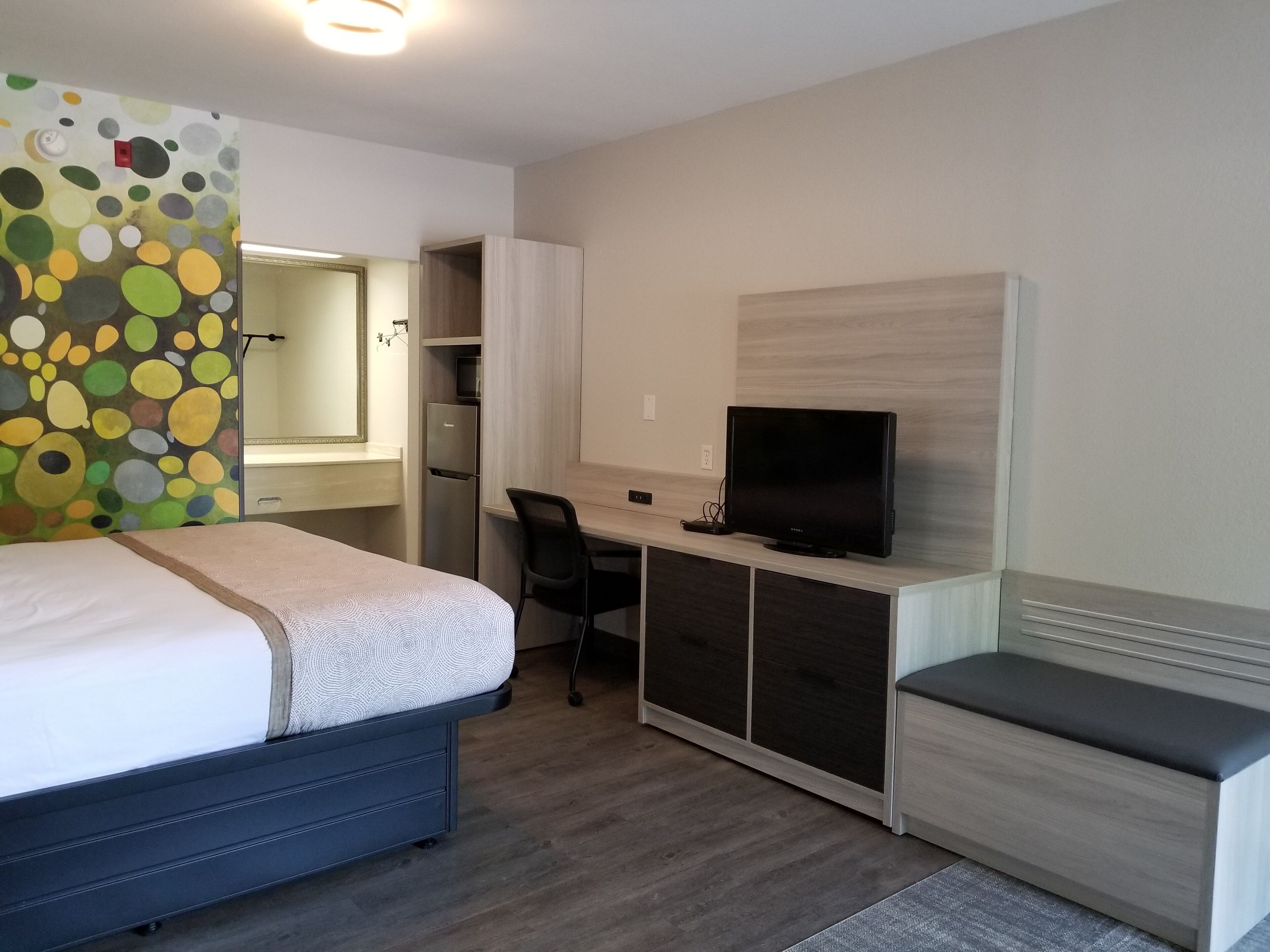 A modern hotel room with a bed, desk, chair, television, and a small seating area.