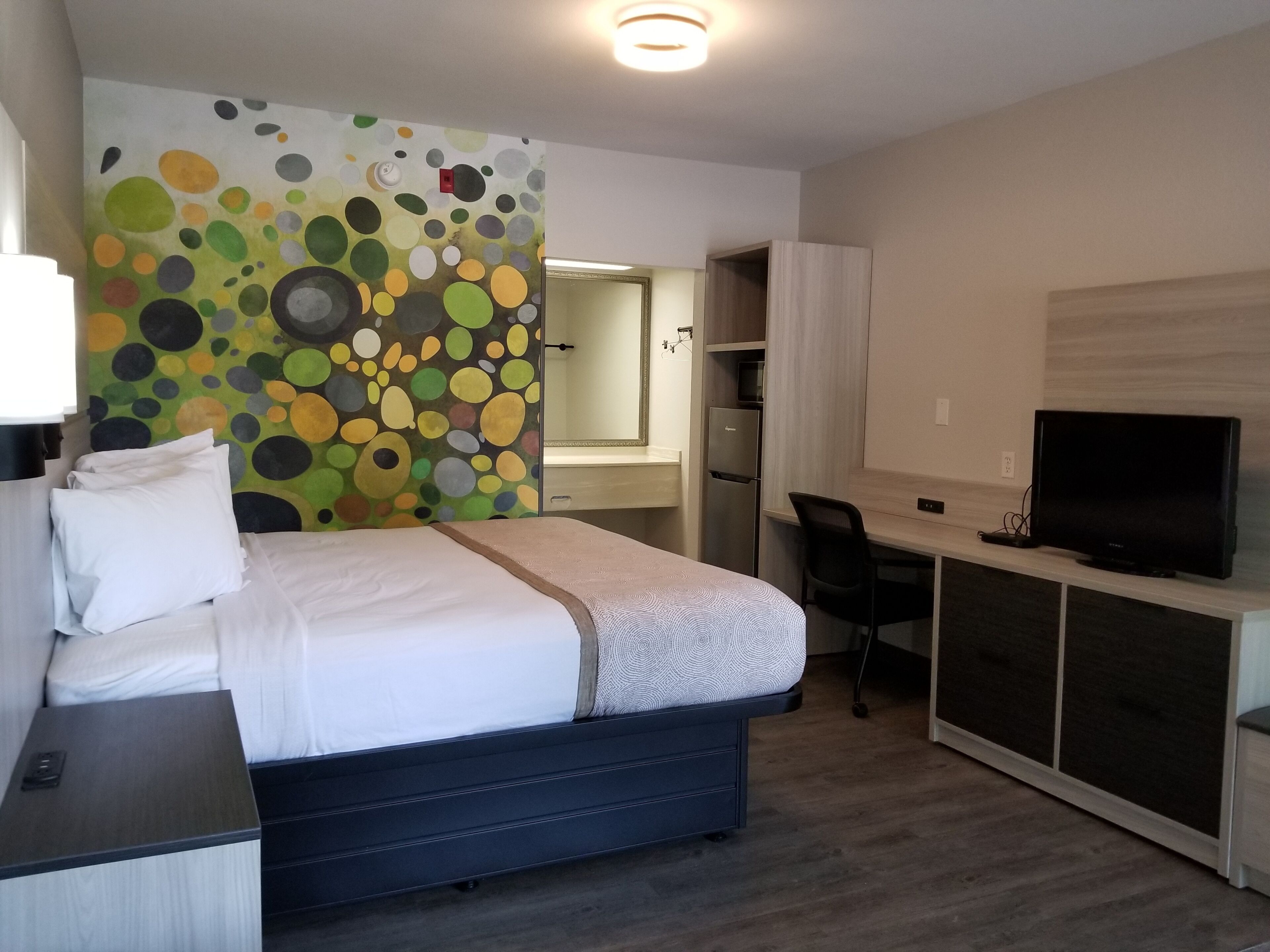 A hotel room with a bed, desk, TV, and a colorful wall.
