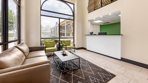 A modern hotel lobby with a leather sofa, green chairs, a black coffee table, and a kitchen area with a green countertop. - The Bradford Hotel, an Ascend Collection Hotel (Springfield)