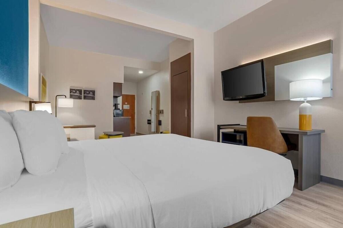 A hotel room with a large bed, a desk with a chair, a television mounted on the wall, and a lamp.