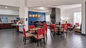 A hotel dining area with multiple tables and chairs, a kitchen area, and a television mounted on the wall. - Comfort Suites Hattiesburg near University (Hattiesburg)