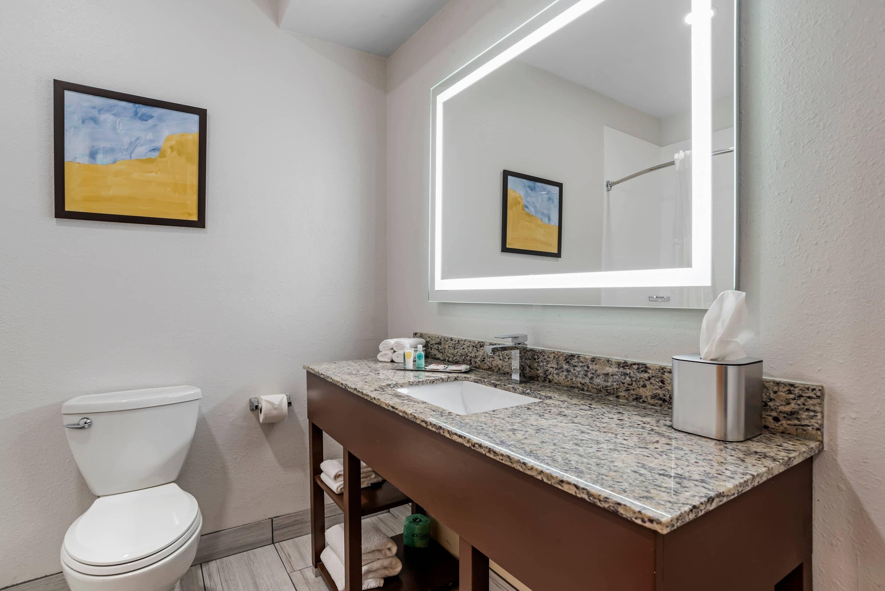 Un baño con inodoro, lavamanos, espejo y perchero para toallas.
