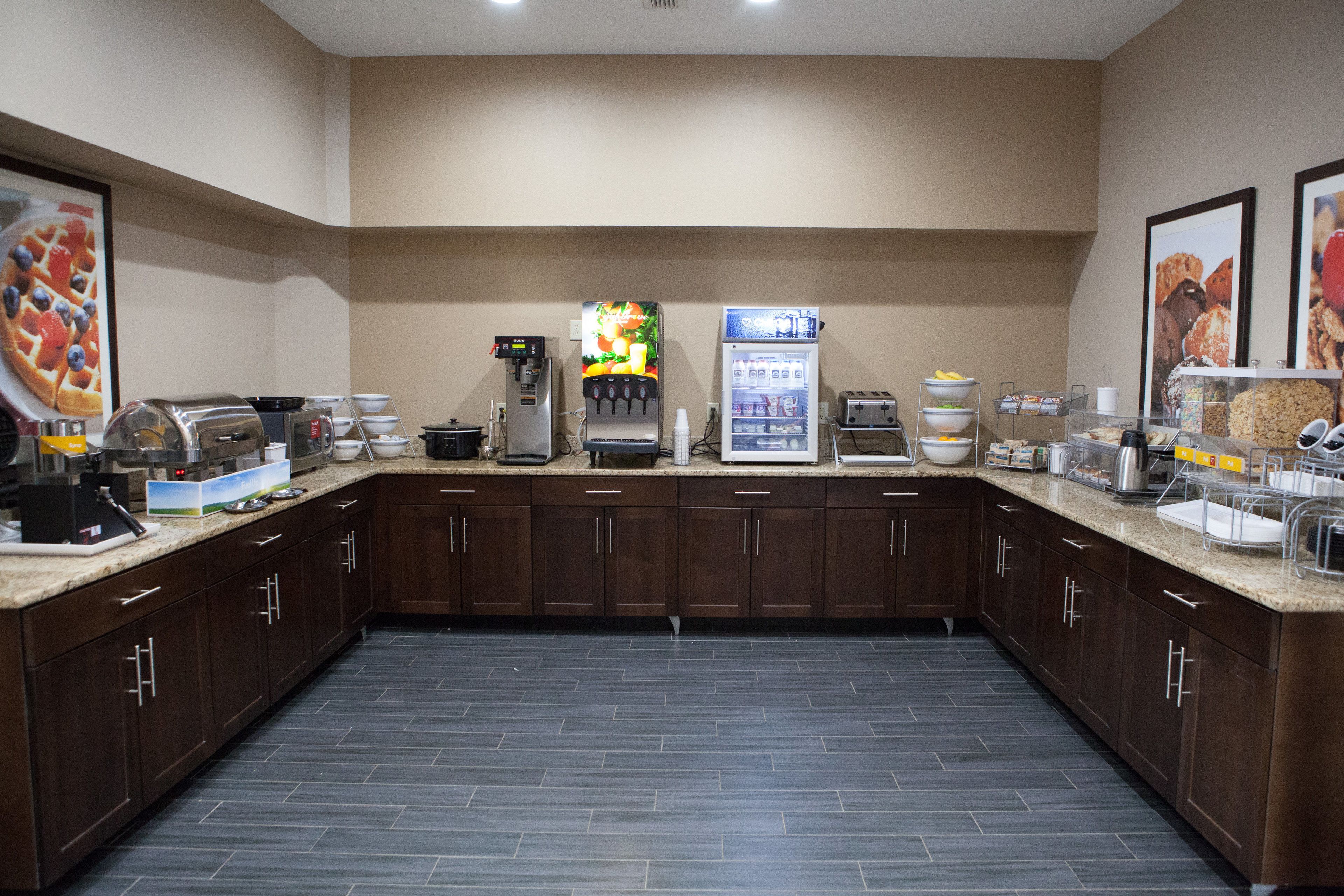 A modern kitchen with dark wood cabinets, a coffee machine, a juice dispenser, and a refrigerator stocked with beverages.