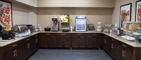 A modern kitchen with dark wood cabinets, a coffee machine, a juice dispenser, and a refrigerator stocked with beverages.