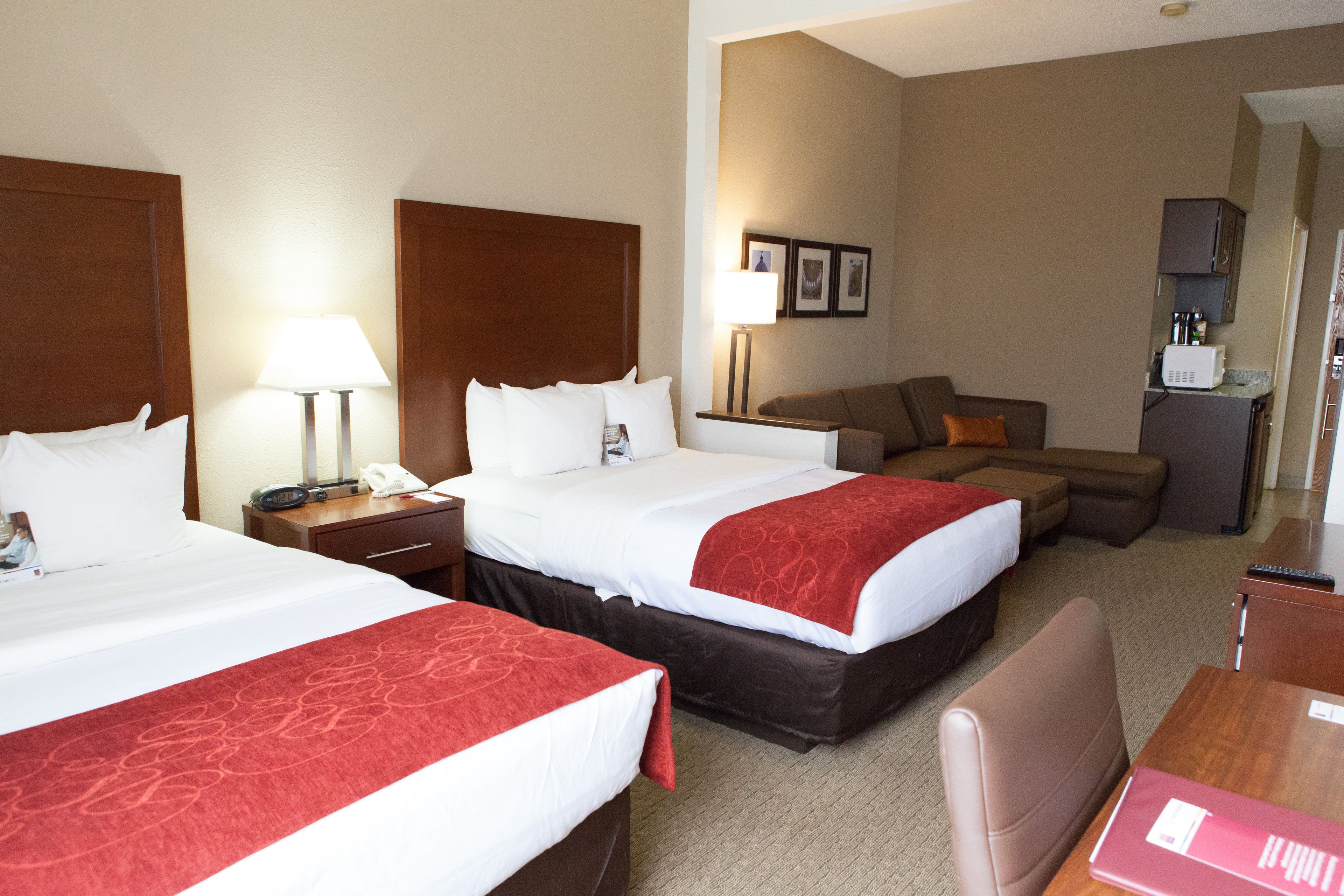 A hotel room with two beds, a sofa, a desk, and a kitchenette.