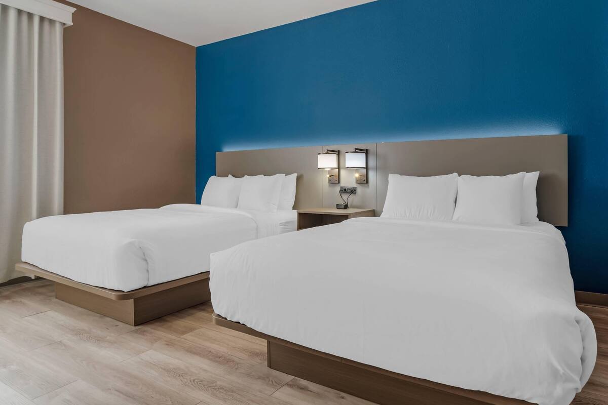 A hotel room with two beds, a nightstand, and a wall-mounted lamp.