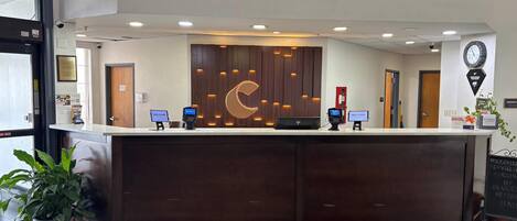 A reception desk with a digital check-in kiosk, a clock, and a welcome sign.