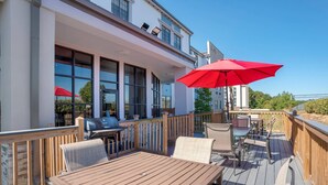 A wooden deck with outdoor furniture, a red umbrella, and a view of a modern building. - Comfort Suites Hattiesburg near University (Hattiesburg)
