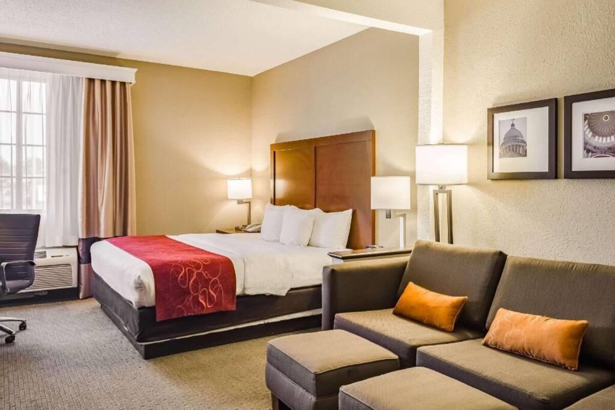 A hotel room with a bed, two bedside lamps, a sofa, a chair, and a framed picture on the wall.