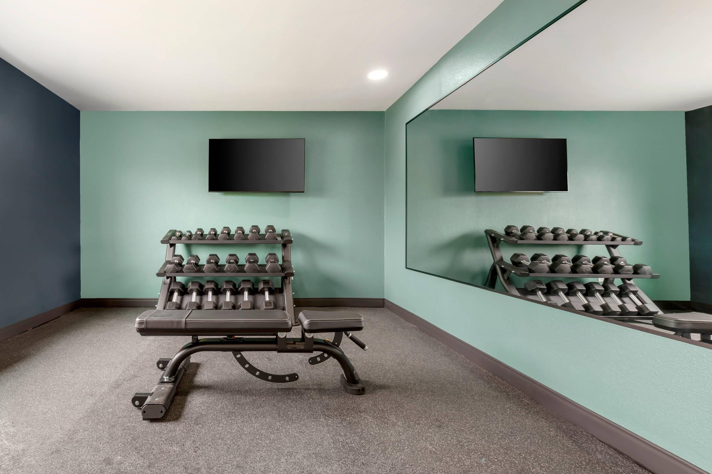 A gym with a mirrored wall, a bench, and a rack of dumbbells.