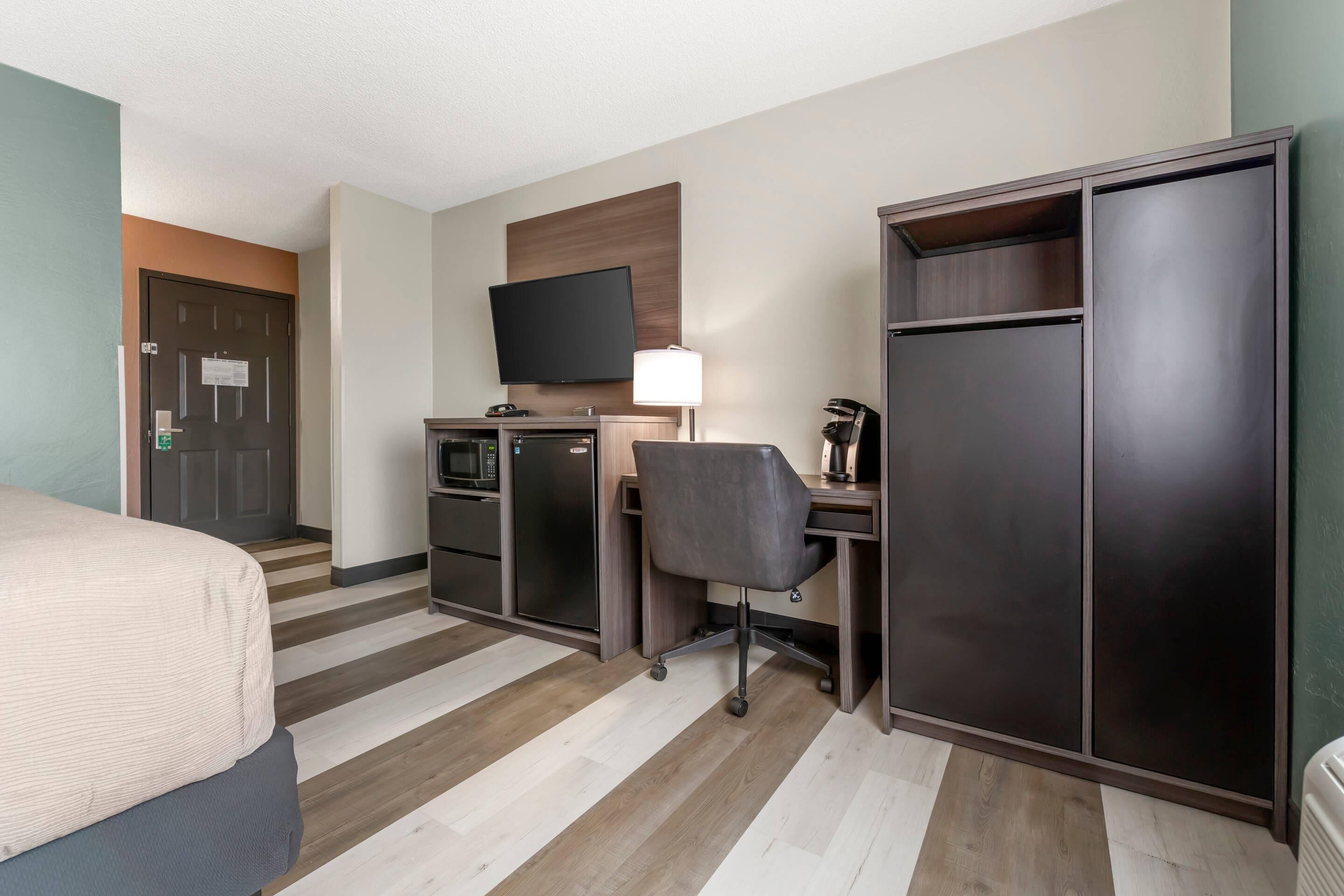 A hotel room with a bed, desk, chair, TV, and wardrobe.