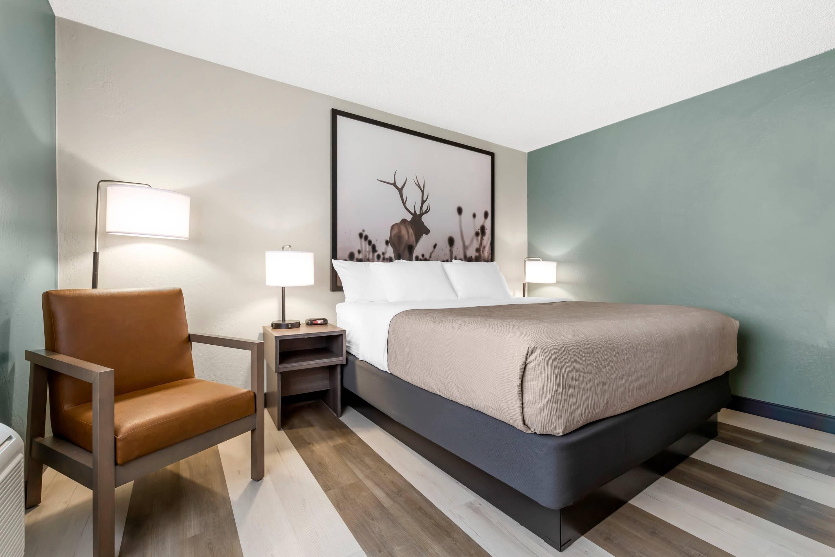 Ein Hotelzimmer mit einem Bett, einem Sessel, zwei Nachttischen und einem Wandbild.