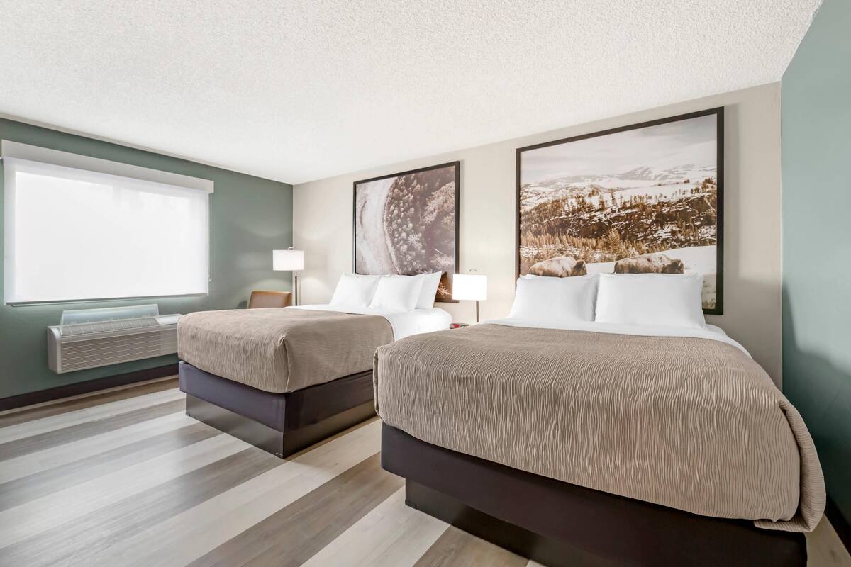 Quarto de hotel com duas camas, uma janela grande e um ar condicionado fixado na parede.