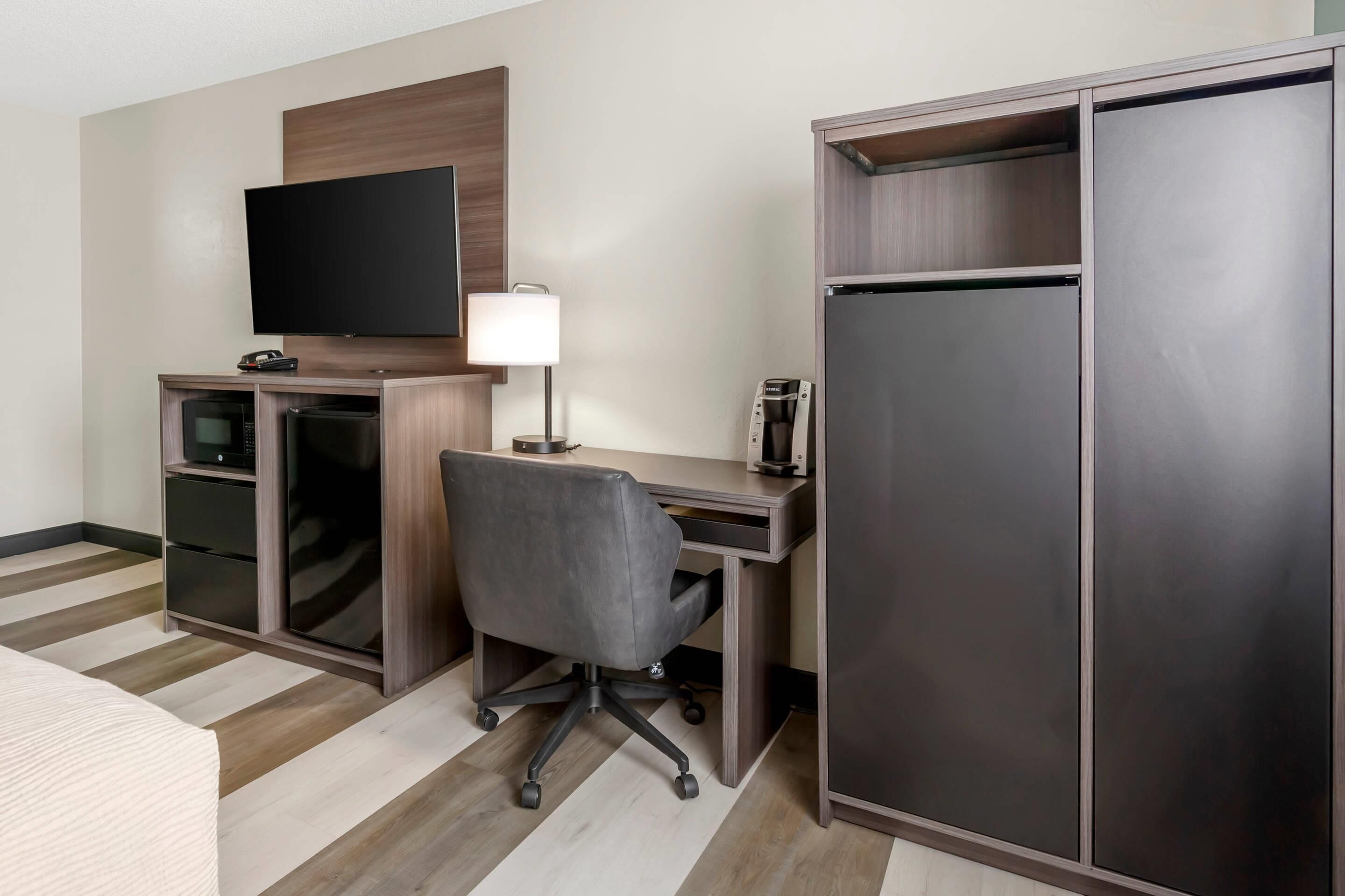 Une chambre d’hôtel équipée d’une télévision à écran plat, d’un bureau avec une chaise, d’un réfrigérateur, d’un four à micro-ondes et d’une machine à café.