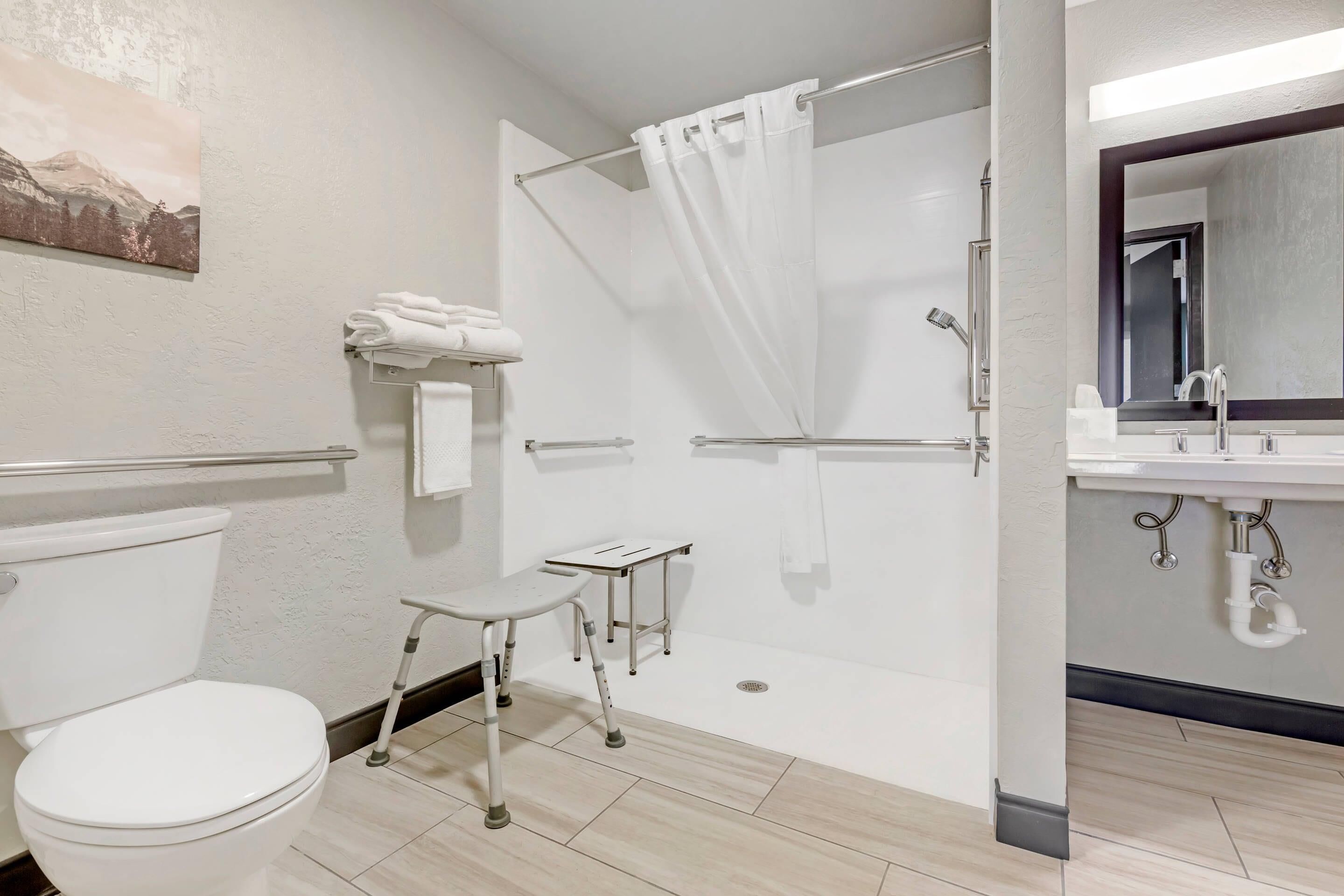A modern bathroom with a toilet, a shower with a glass door, a small table, and a sink with a mirror.