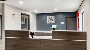 Un comptoir d’accueil d’hôtel avec un revêtement en bois foncé, une enseigne indiquant « Qualité garantie par Choice Hotels » et un écran numérique.