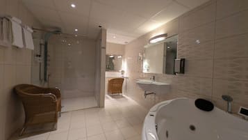 Une salle de bain moderne avec une douche à l’italienne, une baignoire sur pieds, un fauteuil en osier, une commode avec un miroir et un porte-serviettes.