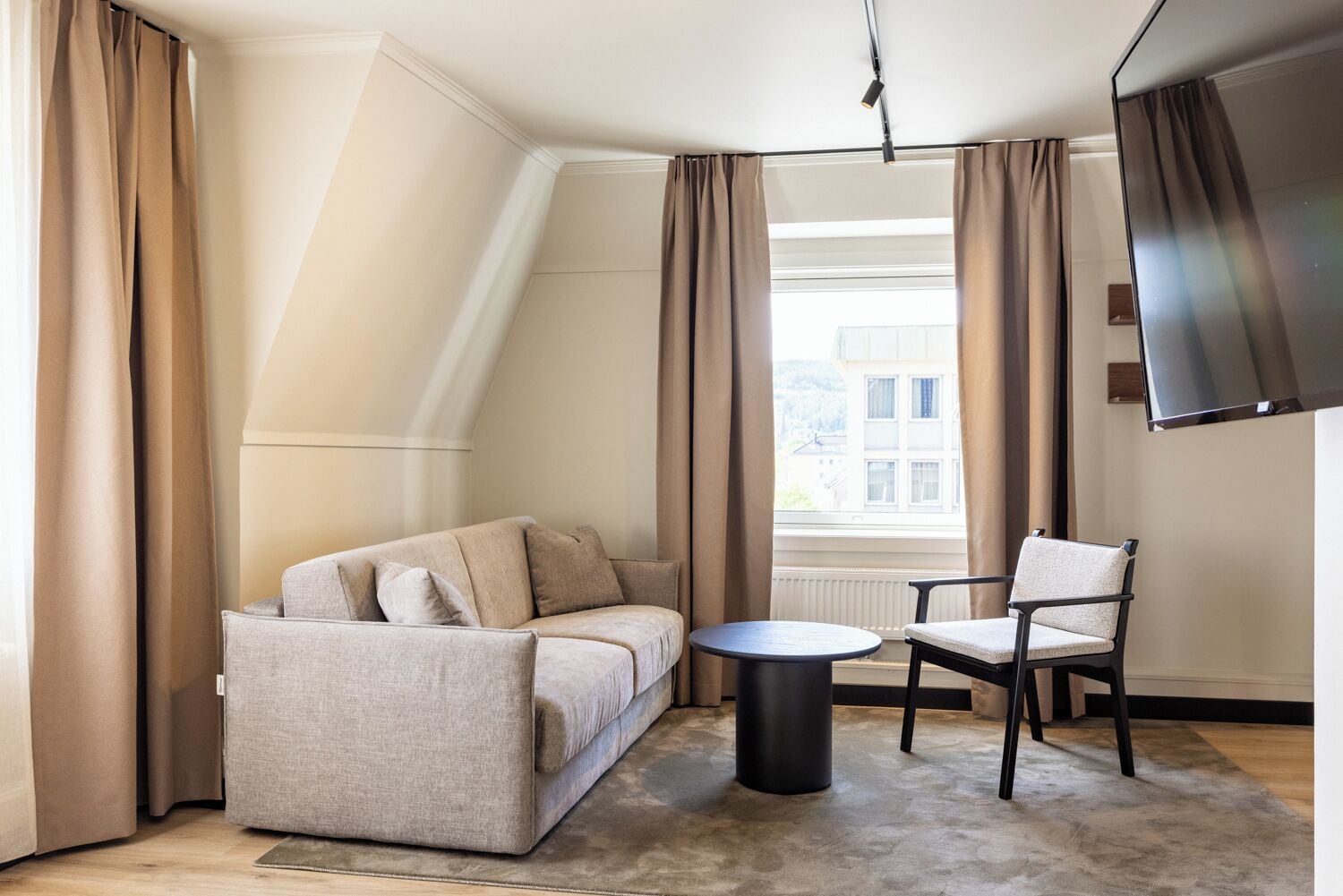 Ein modernes Zimmer mit einer Couch, einem Sessel, einem kleinen Tisch und einem an der Wand befestigten Fernseher.