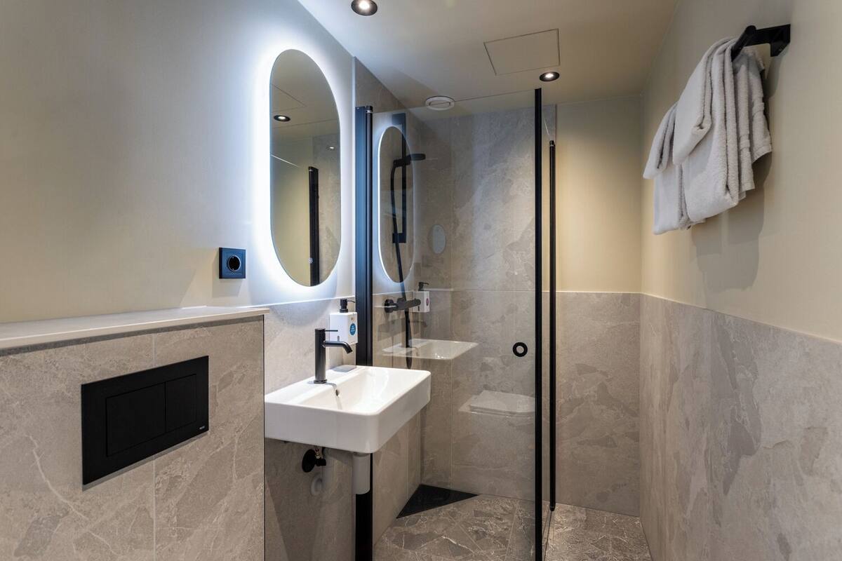 A modern bathroom with a glass-enclosed shower, a white sink, and a large mirror.