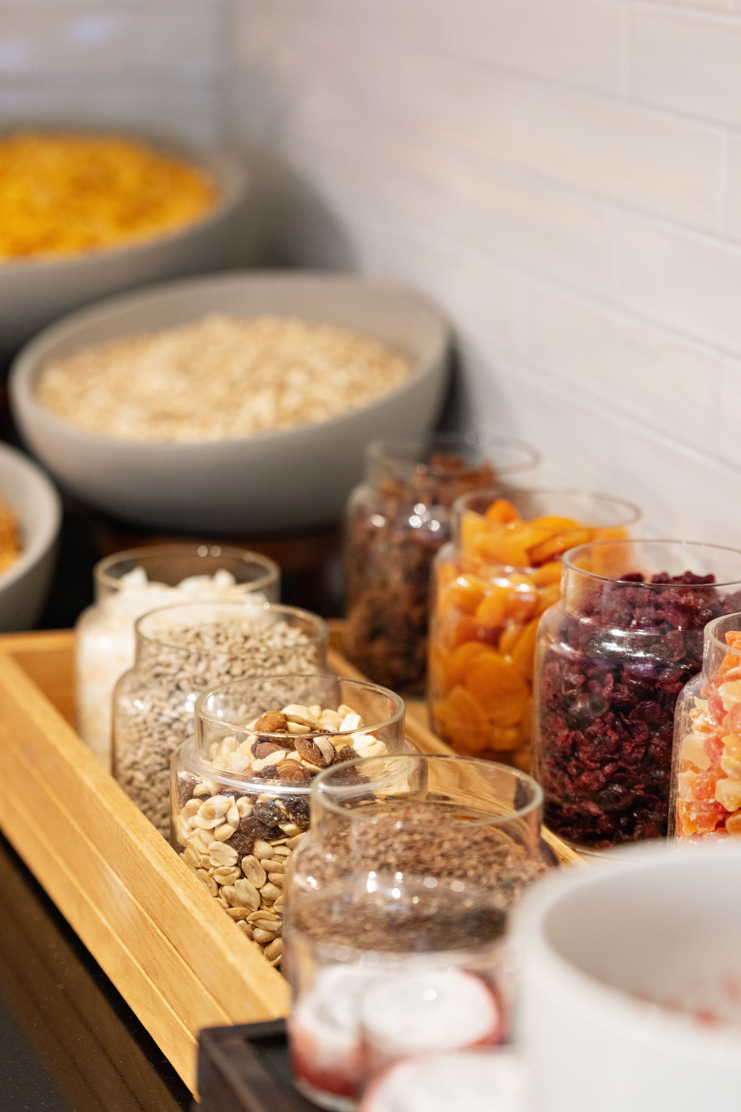 A variety of food items in jars and bowls, including nuts, dried fruits, and grains, displayed on a wooden tray.