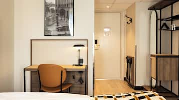 Habitación de hotel con cama, escritorio con silla, lámpara, un cuadro en la pared y piso de madera.