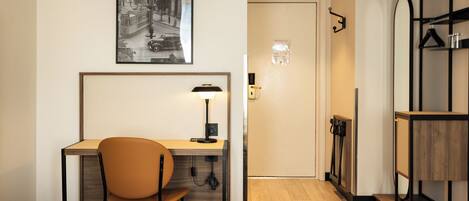 Habitación de hotel con cama, escritorio con silla, lámpara, un cuadro en la pared y piso de madera.