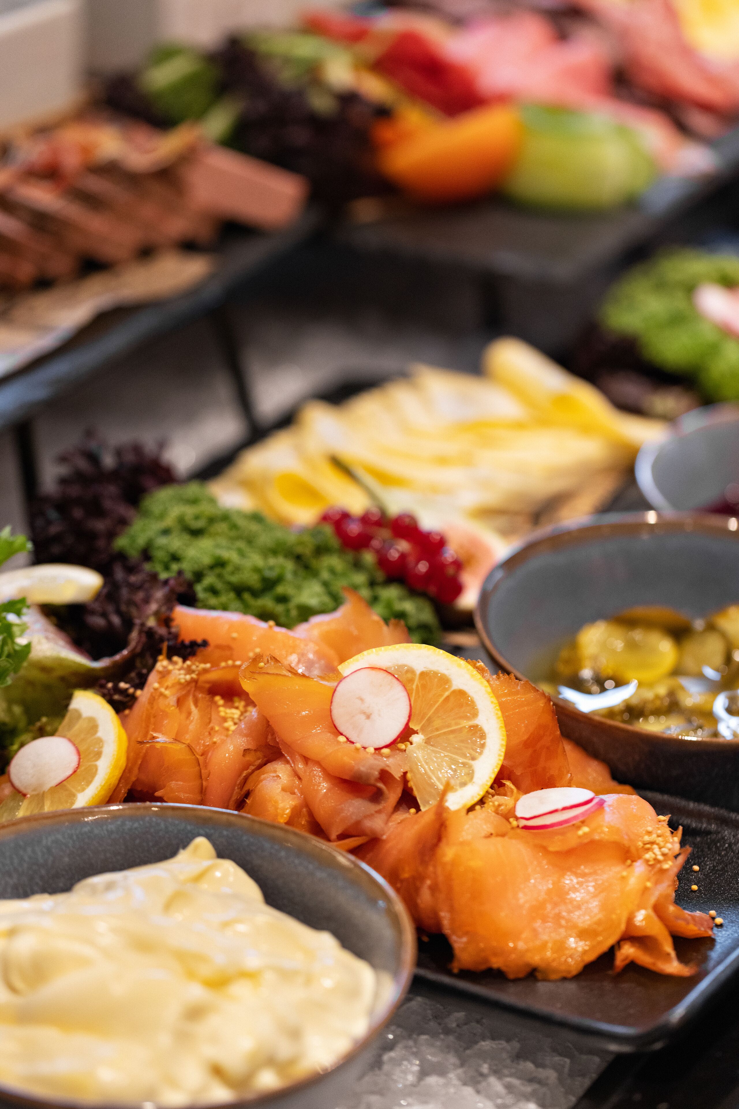 Buffet com diversos pratos, incluindo salmão defumado, legumes e patês.