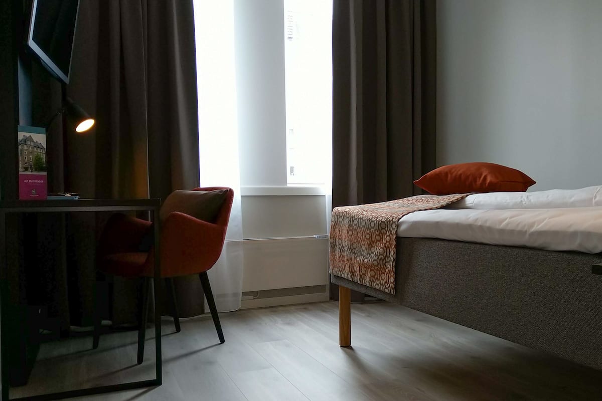 A hotel room with a bed, a desk, a chair, and a window with curtains.