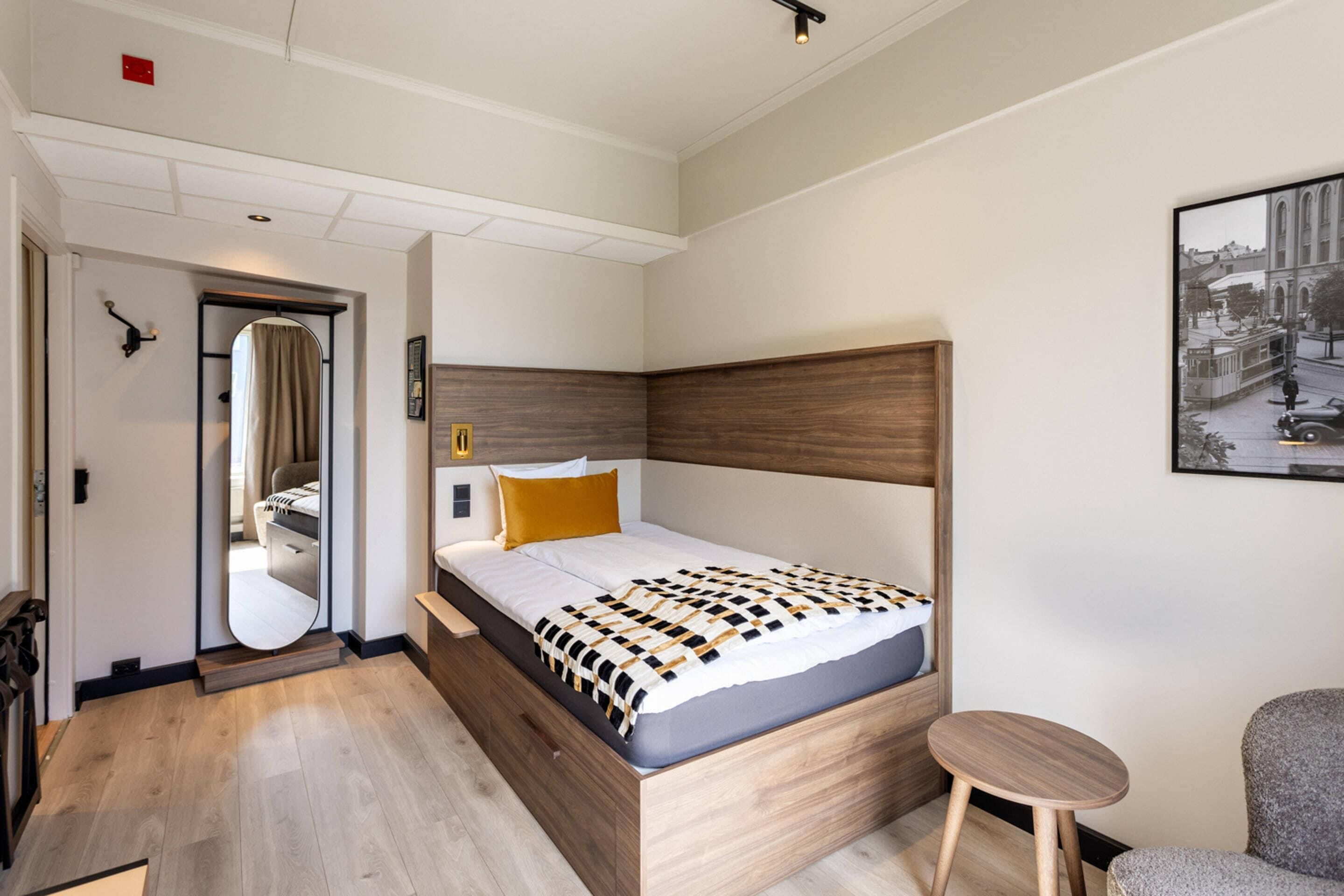 Habitación de hotel con cama, una mesita, un espejo y un cuadro en la pared.