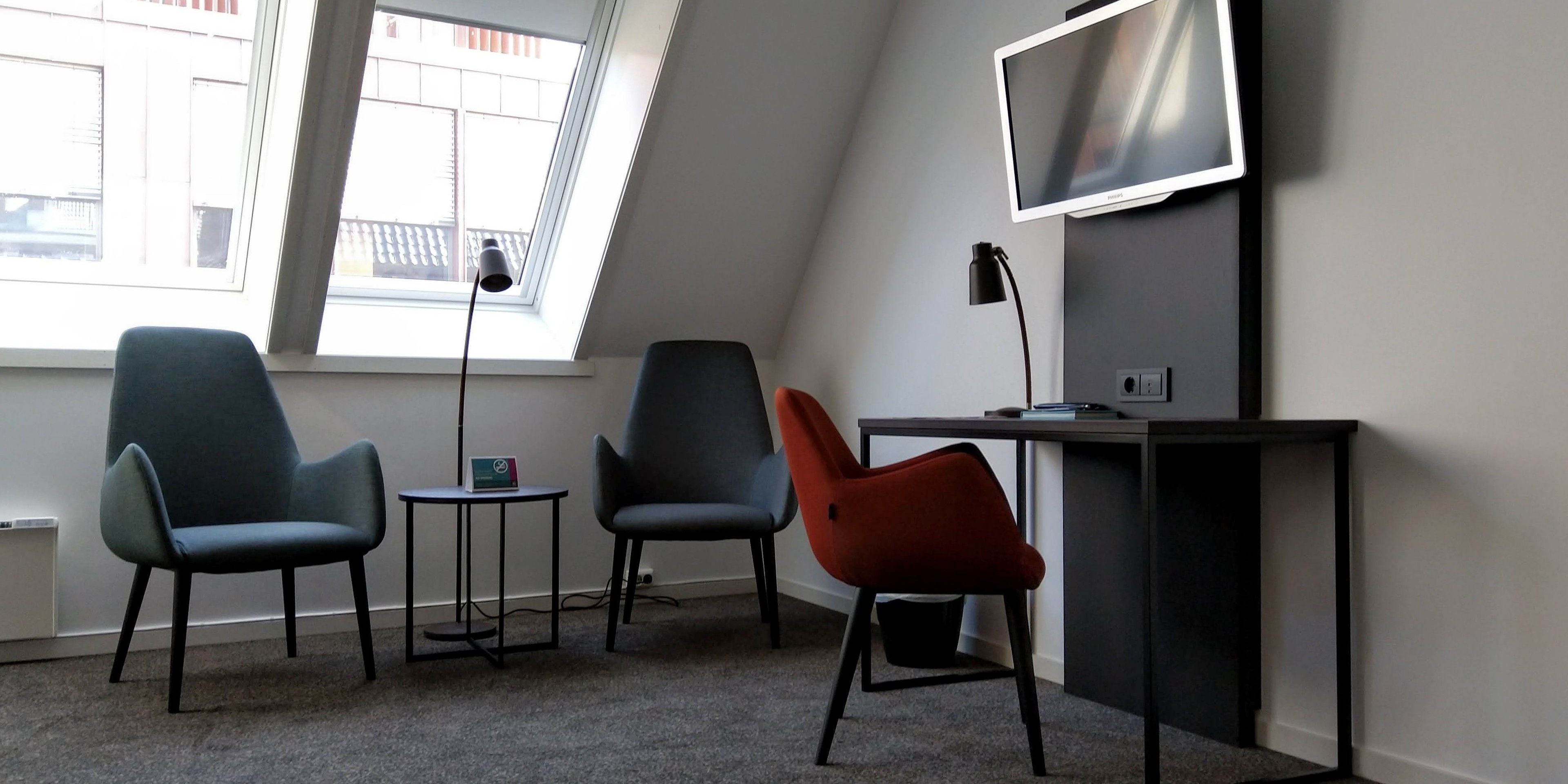 A modern room with a desk, two chairs, a TV, and a window with a view of buildings.