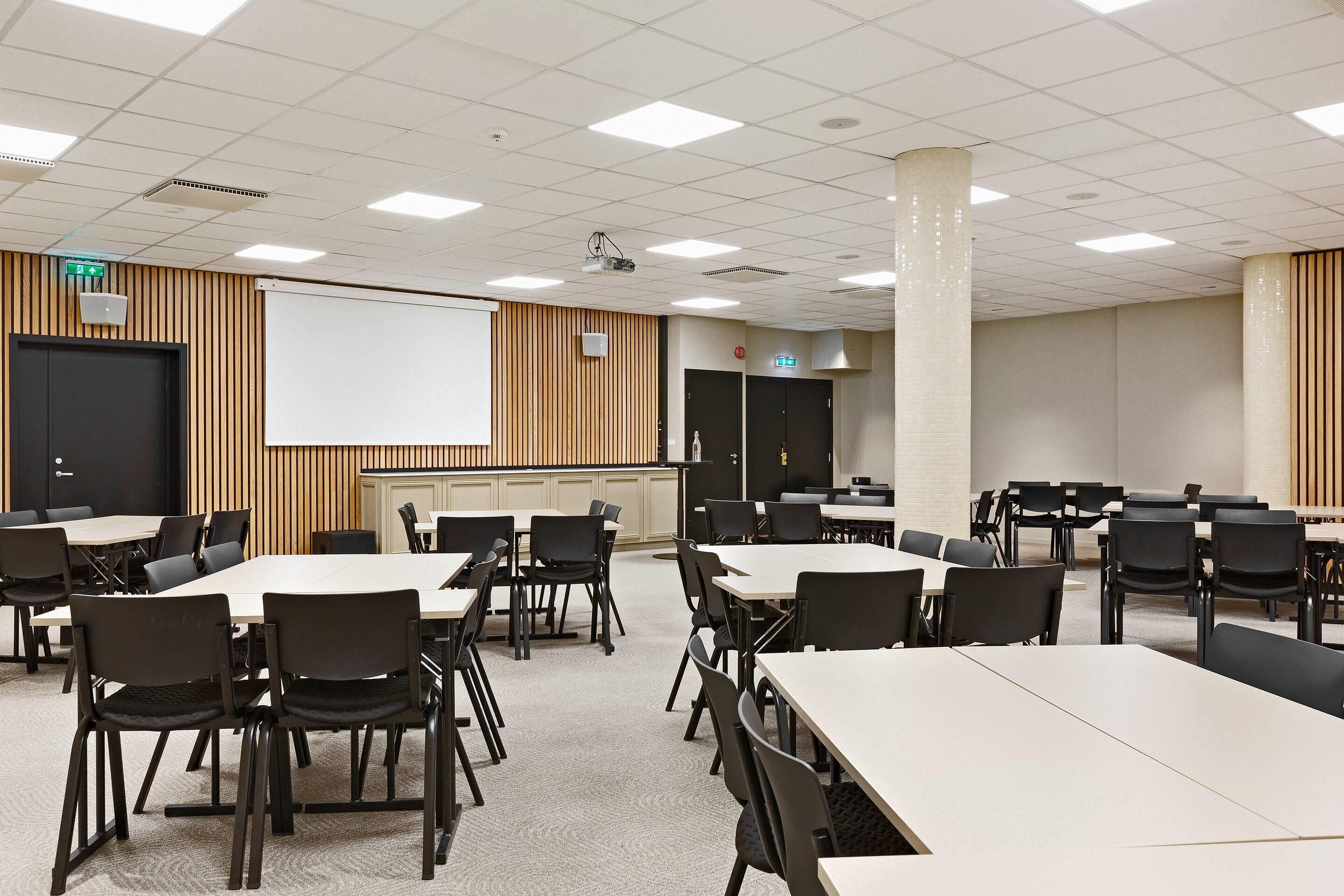 Una sala de conferencias con varias mesas y sillas, una pizarra y un proyector.