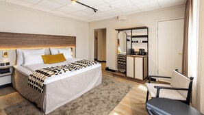 A hotel room with a large bed, a desk with a mirror, a chair, and a wardrobe. - Quality Hotel Augustin (Trondheim)