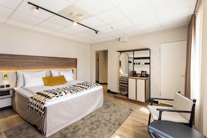 A hotel room with a large bed, a desk with a mirror, a chair, and a wardrobe. - Quality Hotel Augustin (Trondheim)