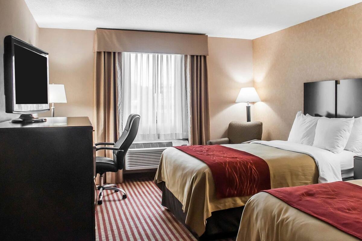 A hotel room with a bed, two bedside tables, a desk with a computer, a chair, a TV, and a window with curtains.