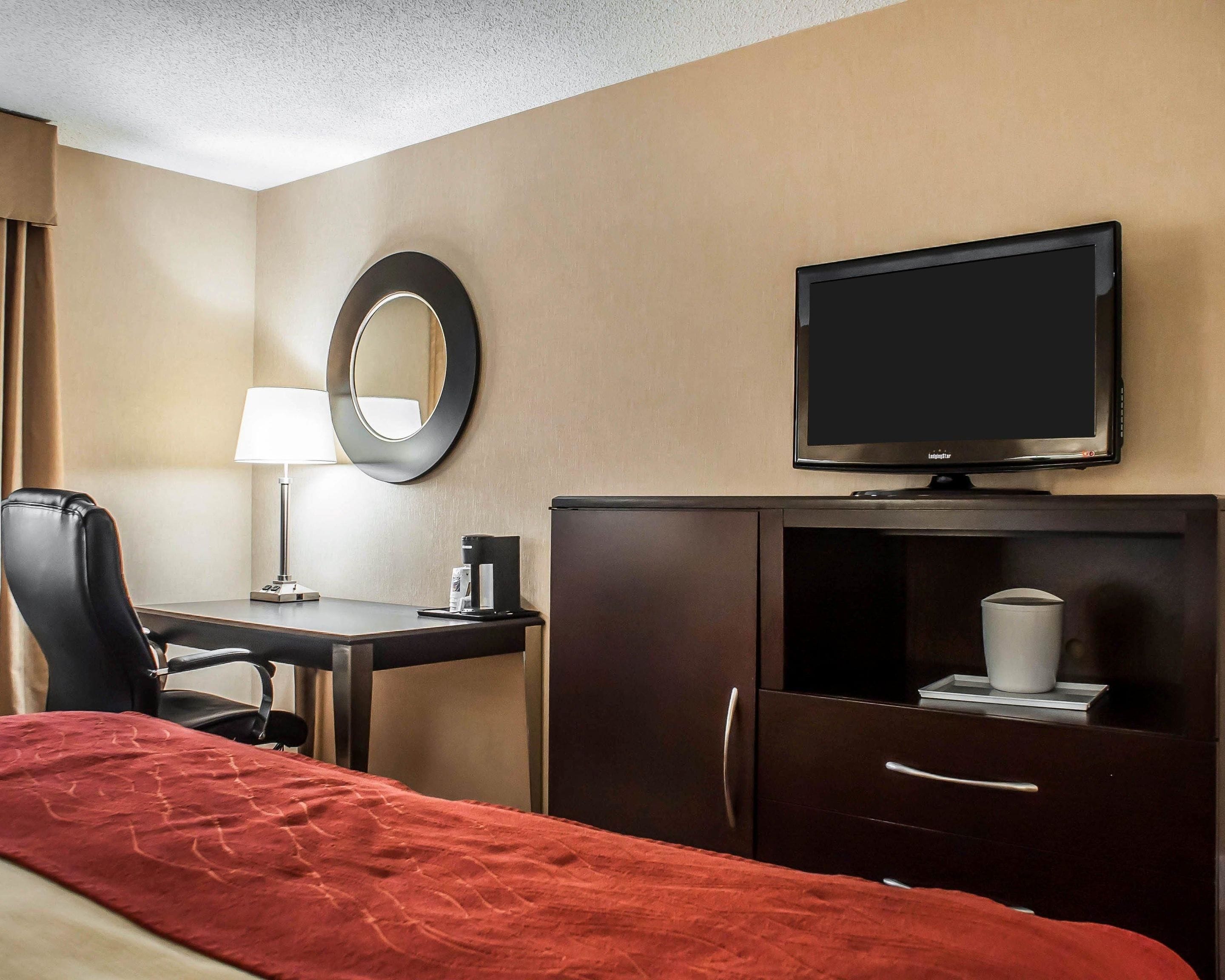 A hotel room with a bed, a desk with a lamp, a television, a mirror, and a wardrobe.