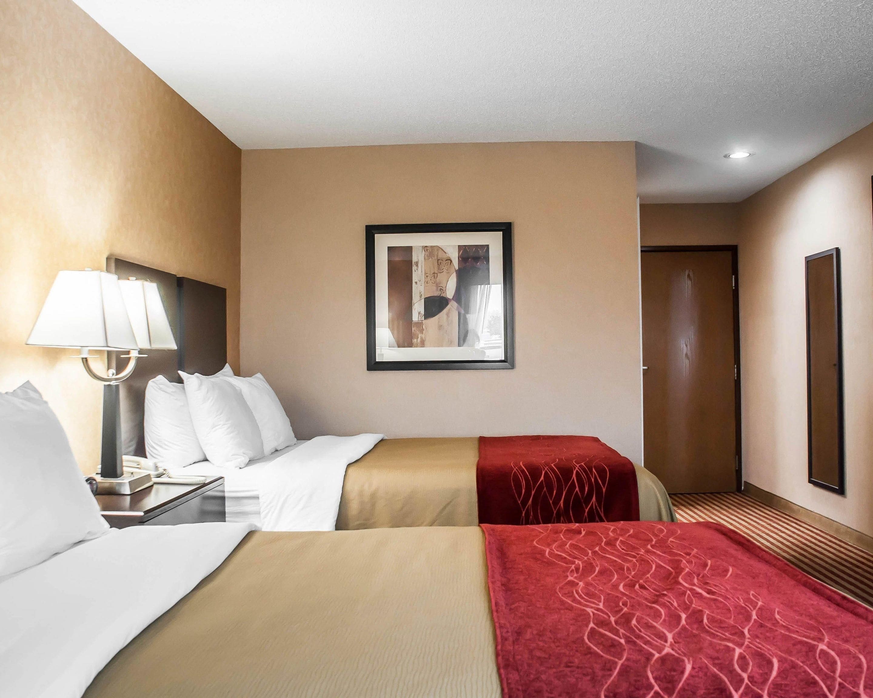 Habitación de hotel con dos camas, una mesita de noche, una lámpara, un cuadro enmarcado en la pared y una puerta.