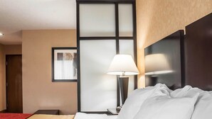 Una habitación de hotel con una cama bien hecha, una lámpara de noche, un cuadro en la pared y una puerta a la izquierda.