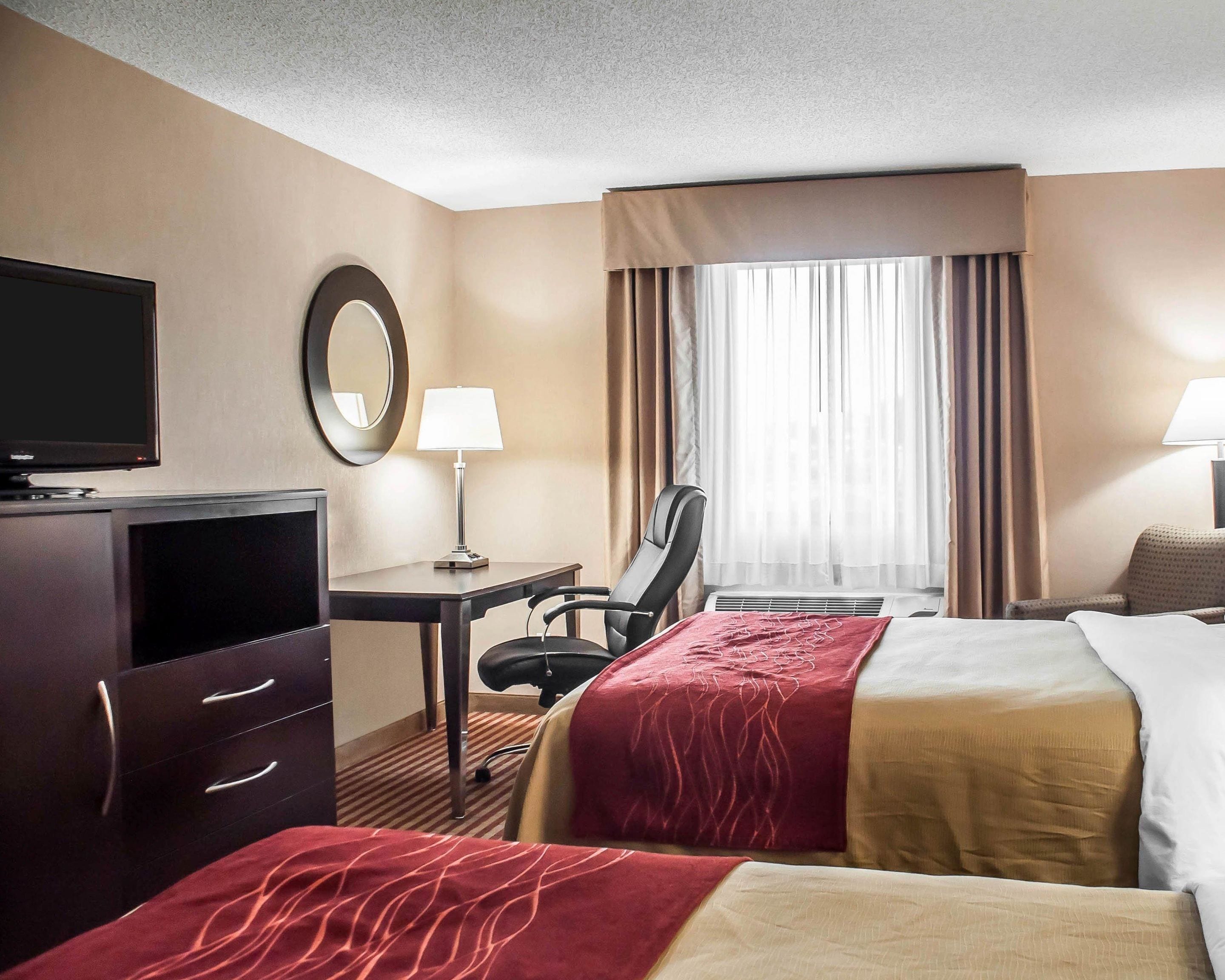 Quarto de hotel com cama, escrivaninha, cadeira, televisão e janela com cortinas.