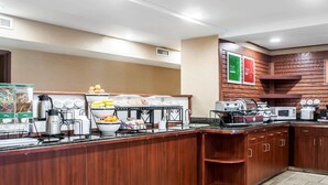 Una mesa de buffet con diversos alimentos y electrodomésticos como una cafetera, microondas y tostadora.