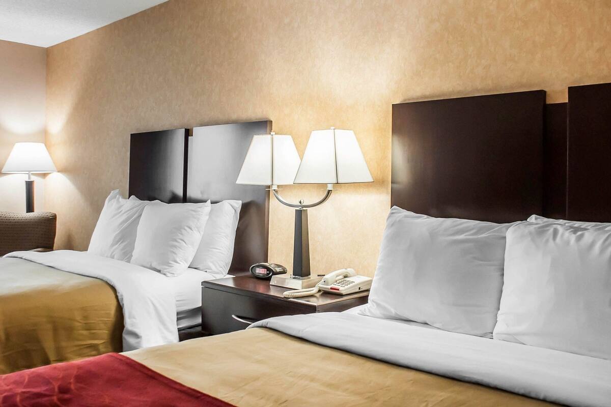 A hotel room with two beds, a nightstand with a lamp, and a telephone.