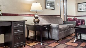 Una habitación de hotel con escritorio, lámpara, sofá y piso alfombrado.